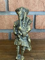 Front view of brass Scottish bagpiper door knocker showing detailed bagpipes and traditional clothing.