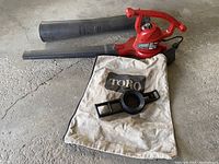 Full view of Toro blower vacuum mulcher with attached blower tube, collection bag, and vacuum inlet adapter on floor surface.