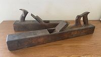 Two antique wooden hand planers, showing their full length and details of wooden handles and blades.