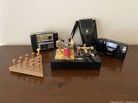 Lot items displayed on wooden surface: two cameras, Nedco table game, wooden peg game, and Waco Japan radio with case.