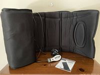 Two black Homedics Destress back massager mats with wired remote controls and power cords displayed on a wooden surface.