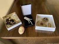 Overall view of six vintage brooches and pendant on dark wooden surface, some in white and black display boxes.