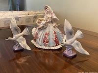 Photo showing the woman figurine with floral dress and two bird figurines on a wooden surface.