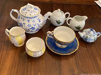 Photo showing full view of the vintage porcelain dish collection, including main teapot, smaller teapots, creamers, sugar bowls, and tea cup set on wooden surface.