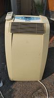 Front view of beige portable air conditioner unit with ventilation grille and control panel on top.