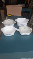 4 vintage Corning Ware dishes and 2 glass lids shown on table