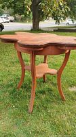 Antique wooden card/poker table with scalloped top and carved legs, placed outdoors on grass.