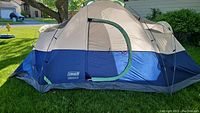 Dome-style tent set up on a grassy lawn, showing beige and dark blue color scheme and zippered door.