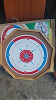Wooden crokinole board with typical scoring rings and holes, colors red, white, blue.