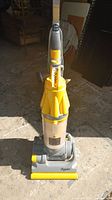 Full front view of yellow Dyson upright vacuum cleaner with clear dust container and yellow accents.