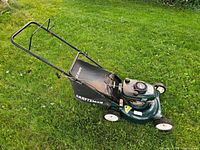 Side view of mower on grass, handle, deck, wheels and grass bag visible