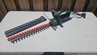 Full view of the Yardworks electric hedge trimmer showing red blade with black protective cover and green body on white table.