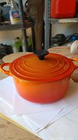 Side view of vintage Le Creuset Dutch oven with visible Flame orange enamel and lid with black knob.