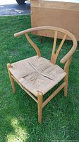 Three-quarter front view of oak frame and woven paper cord seat on grass