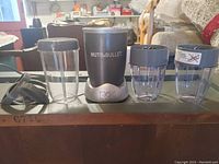 Full view of NutriBullet blender base with two tall containers and two small containers with lids arranged beside it on a table surface.