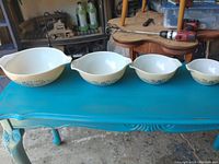 Full set of four Pyrex nesting mixing bowls displayed from largest to smallest on a blue table.