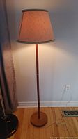 Full view of the teak wood floor lamp illuminated, showing the lamp standing on wooden flooring with its light on.