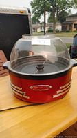 Front view of red retro electric popcorn maker with clear dome lid, showing the power switch and chrome decorative strips.
