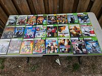 Full overview of all 25 Xbox 360 game cases displayed on a table in two rows, showing colorful covers and titles.