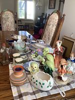 Wide angle photo of the lot displayed on a dining table showing various ceramic and wood figures, salt and peppers, silver plate bowl, and Wedgwood items.