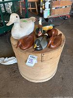 Photo of wooden cheese barrel topped with seven carved wooden ducks, various sizes and finishes, captured in a garage setting.