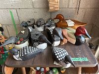 Table displaying a group of 13 wooden bird decoys, primarily loons with one red-headed duck, various sizes and paint details, some with removable backs.