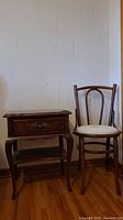 Gibbard nightstand and upholstered wood chair side by side on hardwood floor, wall background.