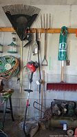 Full view of hanging garden and power tools including Troy-Bilt grass trimmer, Black & Decker hedge trimmer, leaf rake, pitch fork and snow brush.
