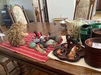 Photo displaying wooden salad bowls, ceramic pitchers, Blue Mountain vase, resin and wooden animal figurines, pepper grinders, and salt and pepper shakers arranged on a dining table.