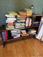 Front view of the wooden bookcase loaded with various books and a cordless phone on top, showing the general condition and book variety