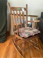 Side view of solid oak rocking chair with floral cushion and visible wear on armrests