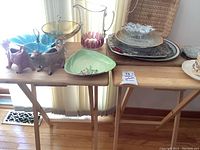 Two wooden TV tables supporting various glass and ceramic serving dishes and decorative items, well lit to show details