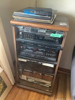 Full view of veneer cabinet with stereo equipment stacked inside and assorted cassettes, CDs and albums on top and inside.