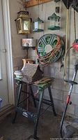 Photo showing the black metal Jobmate folding work table with wooden top, outdoor thermometers hanging above on wall, an assortment of hanging bird feeders and a garden hose reel bracket (hose not included)