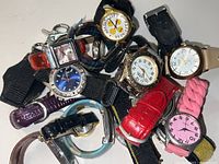 Top view of more than 15 assorted wristwatches piled together, showing a variety of strap colors, materials, and watch face styles.