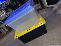 Two stacked plastic storage containers, one translucent with blue lid on top, black with yellow lid on bottom.