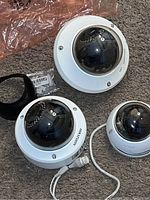 Overview of three dome security cameras varying in size on carpeted surface with plastic shield protection and wiring visible