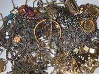 Top-down view of tangled necklaces and bracelets showing mixed gold and silver chains and several pendants including a filigree round pendant and a colorful animal-shaped pendant.