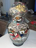 Front view of large glass jar filled with assorted jewelry, wrapped on top in plastic wrap.