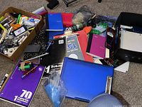 Photo shows notebooks, a blue binder, and various office supplies scattered on a carpeted floor.