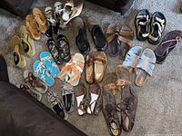 Photo of about 20 pairs of lightly used or new women's and men's shoes of various styles and colors on a carpeted floor.