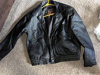 Full front view of vintage black leather men's coat laid flat showing classic styling and condition.