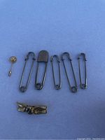 Image showing five large safety pins and two decorative pins on blue background.