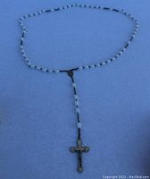 Rosary necklace featuring white beads and a metal cross pendant on a chain, photographed against a flat surface.