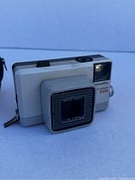 Close side view of white Minolta Togmar 500 camera with detachable lens cover attached, showing camera details and lens branding.