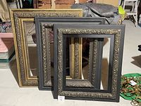 Three ornate decorative picture frames stacked, two black with bronze accents, one bronze with golden edge