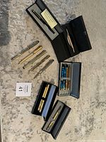 Overview of the pens in cases laid out on carpet, showing a variety of pens including gold-tone and silver-tone