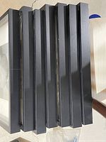 Stack of seven black IKEA Ribba picture frames with flat glass, showing frame thickness and side profile.