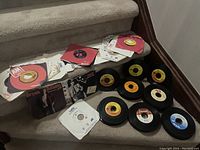 Wide shot of vinyl record singles displayed on stairs and floor with some paper sleeves and record labels visible.