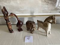 Photo showing four antique carved wooden sculptures including a tall human statue, a swan, an elephant, and a horse arranged on a table